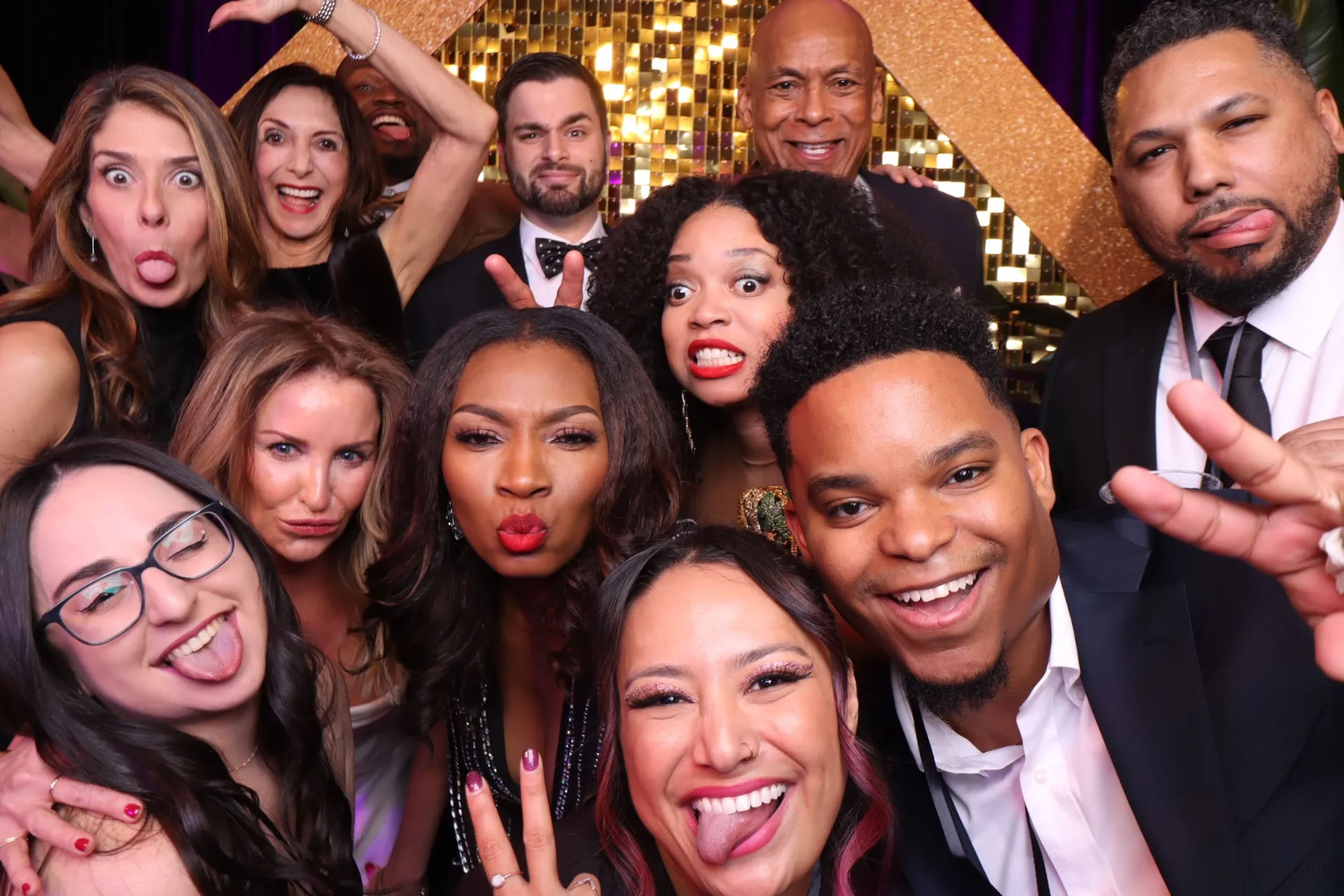 Guests laughing and celebrating at a gold photo-booth backdrop